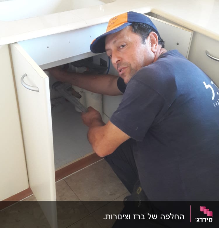 אדם מתקן צנרת מתחת לכיור במטבח